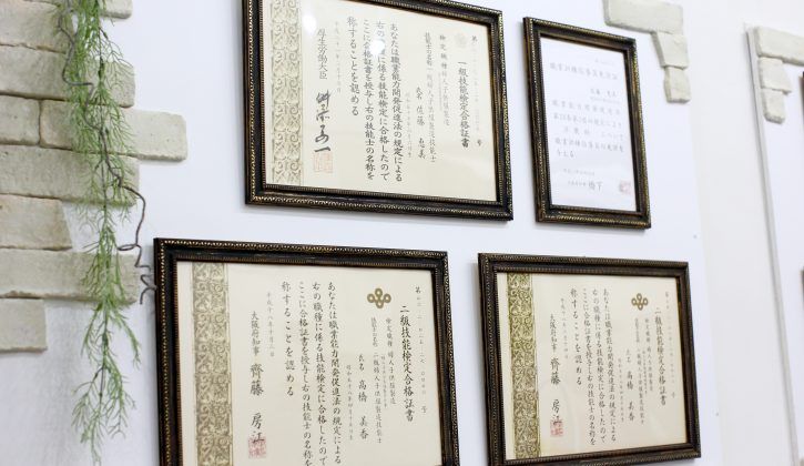 白い壁に、婦人子供服製造の技能検定の合格証書が4枚、額に入れて掛かっている