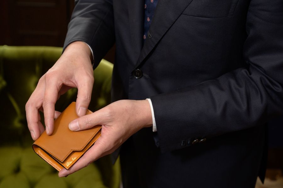 紺のスーツを着た男性が、茶色い革のカードケースを手に持っている